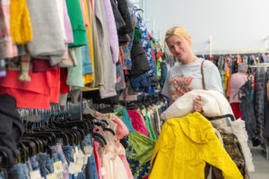 A woman stands beside racks of clothing with several items in her hands
